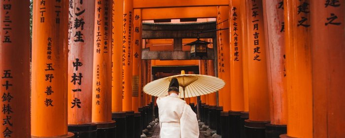 Mann in beiger Kleidung und Schirm läuft durch den Inari Tempel